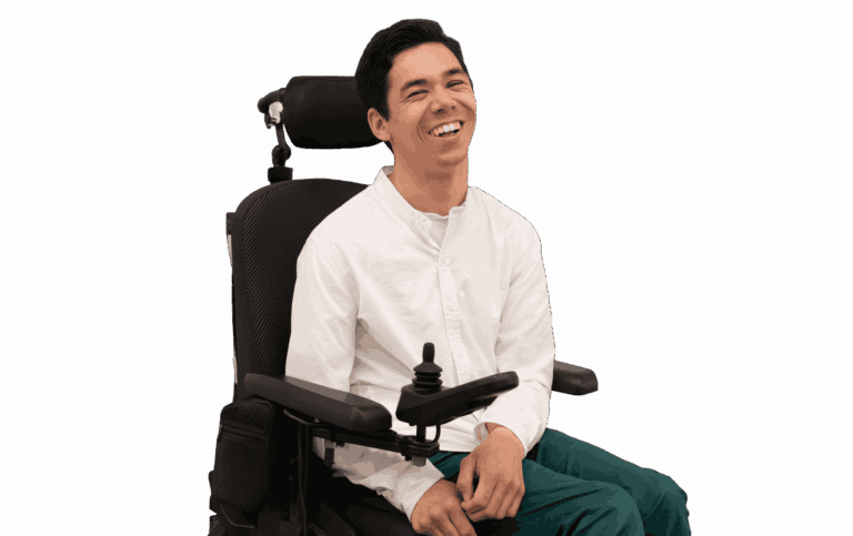 Maarten zittend in zijn elektrische rolstoel. Hij heeft een wit overhemd en, donkergroene broek aan. De foto is van de zijkant genomen en hij lacht.