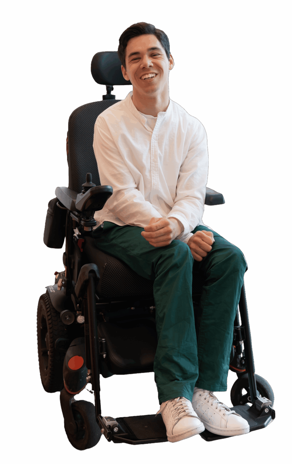 Maarten zittend in zijn elektrische rolstoel. Hij heeft een wit overhemd, donkergroene broek en witte schoenen aan. Hij kijkt recht in de camera en lacht.